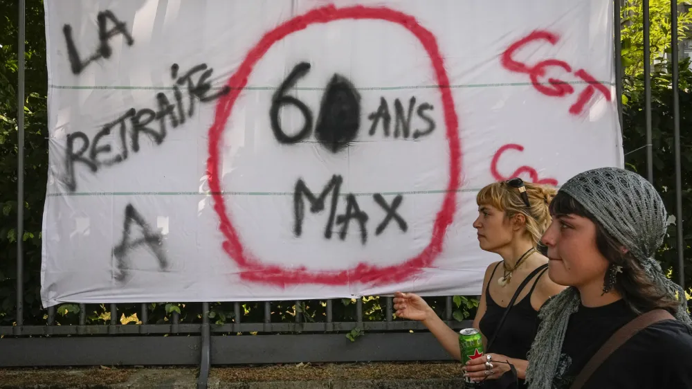 Women pass by a placard that reads: "Retirement age 60 maximum", during a protest in Paris, France, Tuesday, June 6, 2023. French unions are seeking to reignite resistance to President Emmanuel Macron's higher retirement age with what may be a final surge of nationwide protests and scattered strikes Tuesday. (AP Photo/Michel Euler)