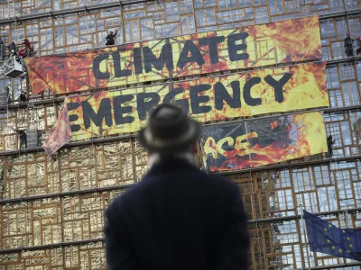 ﻿A man looks up as police and fire personnel move in to remove climate activists after they climbed the Europa building during a demonstration outside an EU summit meeting in Brussels, Thursday, Dec. 12, 2019. Greenpeace activists on Thursday scaled the European Union's new headquarters, unfurling a huge banner warning of a climate emergency hours before the bloc's leaders gather for a summit focused on plans to combat global warming.(AP Photo/Francisco Seco)