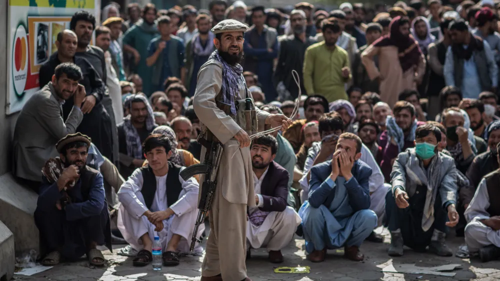 FILED - 22 September 2021, Afghanistan, Kabul: A Taliban security guard plays with a whip while standing in front of Afghan men waiting outside a bank to withdraw money. More than 1,000 civilians have been killed in Afghanistan since the Taliban returned to power in August of 2021, a United Nations report released on Tuesday shows. Photo: Oliver Weiken/dpa