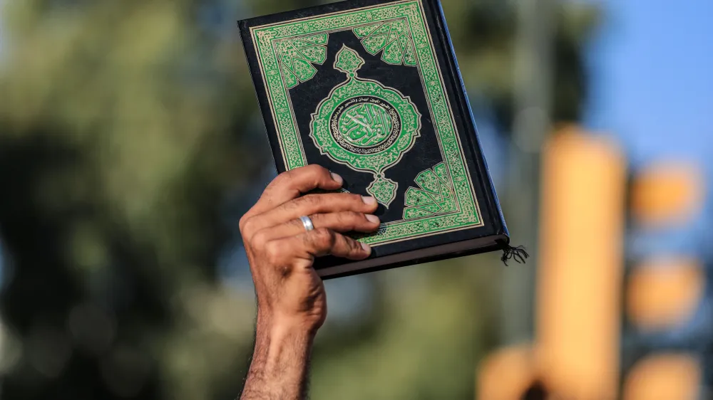 30 June 2023, Iraq, Baghdad: A man rises a copy of Islam's holy book, the Quran, during a protest against the burning a copy of the Quran in Sweden. Photo: Ameer Al-Mohammedawi/dpa