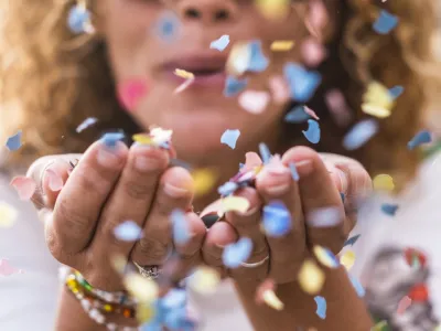 beautiful defocused woman blow confetti from hands. celebration and event concept. happiness and colored image. movement and happiness having fun