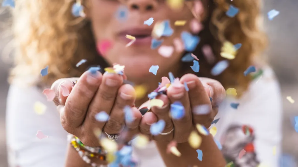 beautiful defocused woman blow confetti from hands. celebration and event concept. happiness and colored image. movement and happiness having fun