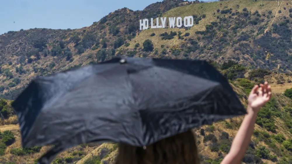 Tourists take pictures under an umbrella at the Griffith Observatory in Los Angeles Friday, July 14, 2023. Over a third of Americans are under extreme heat advisories, watches, and warnings as a blistering heatwave continues across the Southwest and California. The sweltering conditions were expected to keep building Friday and through the weekend. Forecasters say some California residents should prepare for the hottest weather of the year. (AP Photo/Damian Dovarganes)