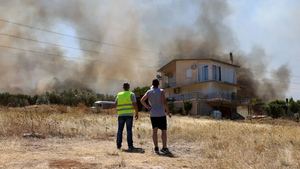 People stand in front of a house, as a wildfire burns in Kouvaras, Greece, July 17, 2023. REUTERS/Stelios Misinas   TPX IMAGES OF THE DAY