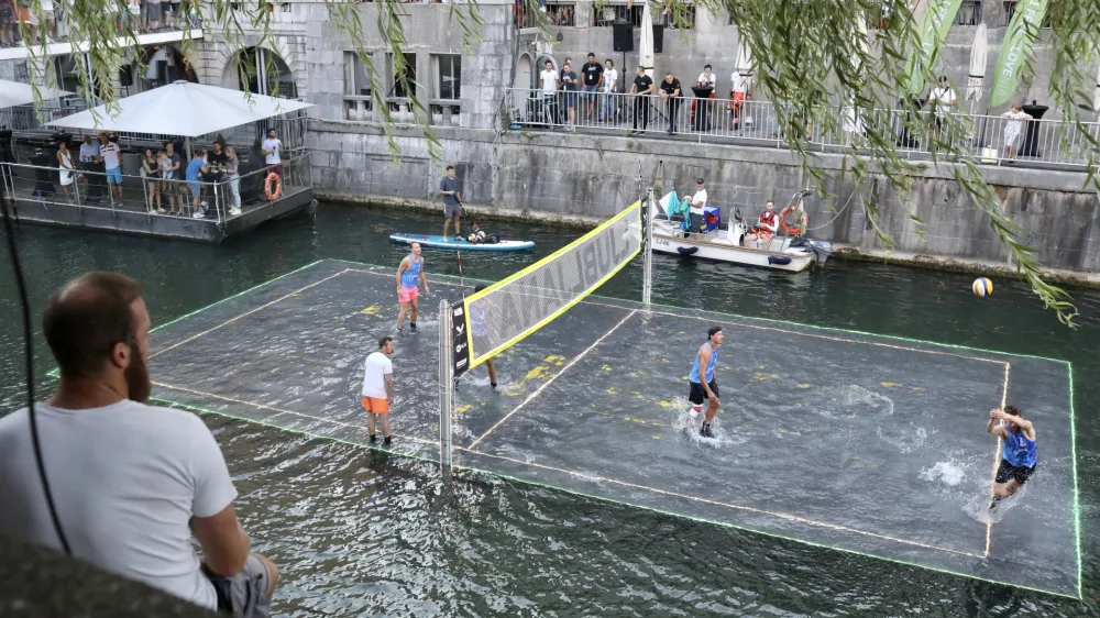 16.08.2022 - Ljubljana: Odbojkarski spektakel na vodi<br>Platforma na reki z igriščem dimenzij 7 krat 14 metrov je potopljena 10 centimetrov pod vodno gladino, igrišče pa je označeno s svetlobnimi črtami.<br>
