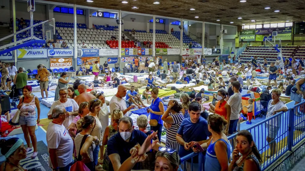 Evacuees sit inside a stadium following their evacuation during a forest fire on the island of Rhodes, Greece, Sunday, July 23, 2023. Some 19,000 people have been evacuated from the Greek island of Rhodes as wildfires continued burning for a sixth day on three fronts, Greek authorities said on Sunday. (Argyris Mantikos/Eurokinissi via AP)