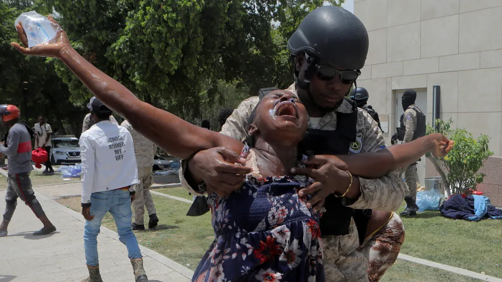 An officer of the Haitian National Police holds a woman affected by tear gas after the police cleared a camp of people escaping the threat of armed gangs, in front of the U.S. Embassy, in Port-au-Prince, Haiti July 25, 2023. REUTERS/Ralph Tedy Erol