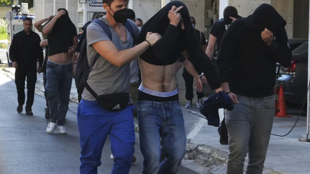 Soccer fans covering their faces, most of them from Croatia, are escorted by police as they leave the Athens Police Headquarters, Greece, Wednesday, Aug. 9, 2023. Ninety-four fans of Croatia's Dinamo Zagreb are appearing in court this morning for a preliminary hearing over Monday night's fan violence that left a fan of Greece's AEK dead and another eight people injured. (AP Photo/Petros Giannakouris)