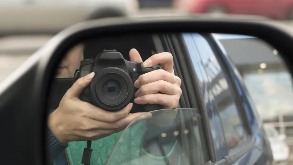 Hidden photographing. Reflection in car mirror of woman with camera. Paparazzi concept