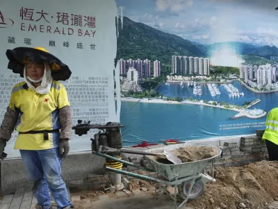 A worker walks past an advertisement photo of a property project of China Evergrande Group outside its headquarters in Hong Kong Monday, Oct. 4, 2021. Shares in troubled real estate developer China Evergrande Group and its property management unit Evergrande Property Services were suspended from trading Monday in Hong Kong. (AP Photo/Vincent Yu)