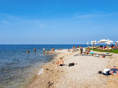 Izo, Slovenia – February 04, 2021: People on beach in Izola, Slovenia. Sunny summer day, palm trees, city, town, horizon, sea, vacation, travel.
