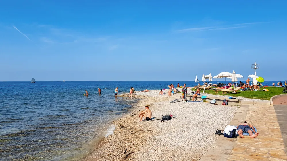 Izo, Slovenia – February 04, 2021: People on beach in Izola, Slovenia. Sunny summer day, palm trees, city, town, horizon, sea, vacation, travel.