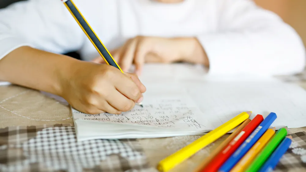 Child doing homework and writing story essay. Elementary or primary school class. Closeup of hands and colorful pencils.