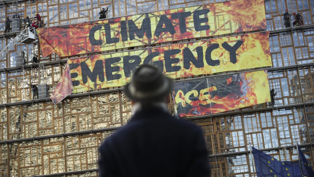 ﻿A man looks up as police and fire personnel move in to remove climate activists after they climbed the Europa building during a demonstration outside an EU summit meeting in Brussels, Thursday, Dec. 12, 2019. Greenpeace activists on Thursday scaled the European Union's new headquarters, unfurling a huge banner warning of a climate emergency hours before the bloc's leaders gather for a summit focused on plans to combat global warming.(AP Photo/Francisco Seco)