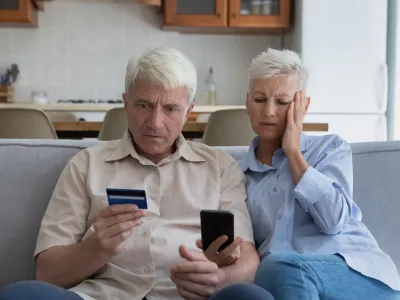 Shocked aged couple become victims of online fraud using credit card phone to pay for goods order service online on suspicious website. Frustrated older spouses overspending money at internet shopping