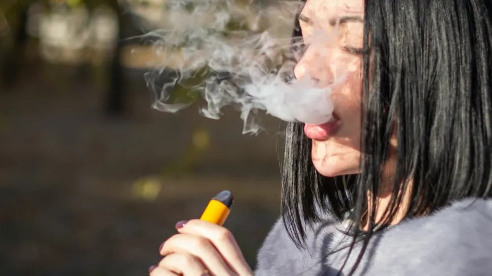 The girl smokes an electronic cigarette on the street.