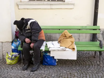 Homeless man in dirty clothes sleeps on a green bench in the center of Ljubljana, Slovenia.