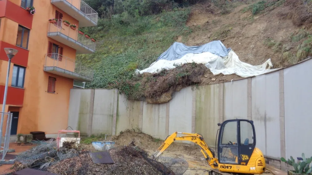 Delavci odstranjujejo približno 25 metrov dolgo plazino in utrjujejo brežino ob bloku. 