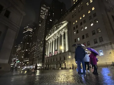 File - People huddle outside the New York Stock Exchange on Tuesday, Nov. 21, 2023 in New York. (AP Photo/Peter Morgan, File)