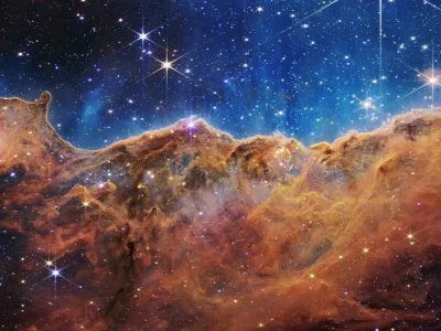 The "Cosmic Cliffs" of the Carina Nebula is seen in an image divided horizontally by an undulating line between a cloudscape forming a nebula along the bottom portion and a comparatively clear upper portion, with data from NASA's James Webb Space Telescope, a revolutionary apparatus designed to peer through the cosmos to the dawn of the universe and released July 12, 2022. Speckled across both portions is a starfield, showing innumerable stars of many sizes.  NASA, ESA, CSA, STScI, Webb ERO Production Team/Handout via REUTERS THIS IMAGE HAS BEEN SUPPLIED BY A THIRD PARTY.