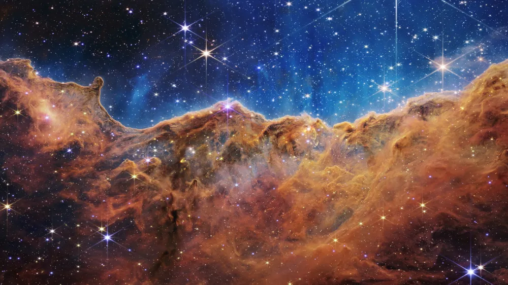 The "Cosmic Cliffs" of the Carina Nebula is seen in an image divided horizontally by an undulating line between a cloudscape forming a nebula along the bottom portion and a comparatively clear upper portion, with data from NASA's James Webb Space Telescope, a revolutionary apparatus designed to peer through the cosmos to the dawn of the universe and released July 12, 2022. Speckled across both portions is a starfield, showing innumerable stars of many sizes.  NASA, ESA, CSA, STScI, Webb ERO Production Team/Handout via REUTERS THIS IMAGE HAS BEEN SUPPLIED BY A THIRD PARTY.