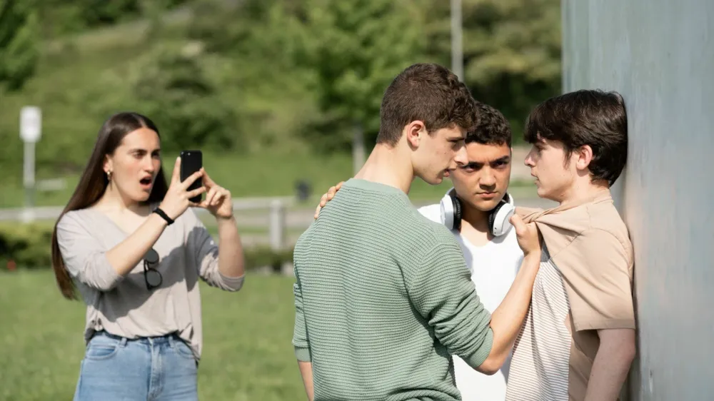 Two bullies menacing teenager boy and girl filming on phone. Cyber bullying and violence concept.