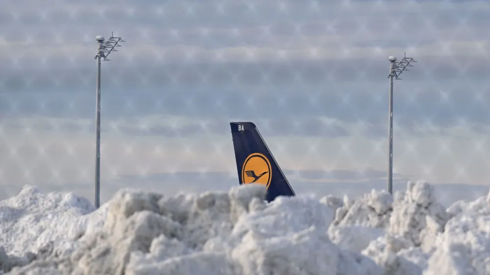 A tail fin of a Lufthansa plane is pictures behind snow at the terminal as Munich Airport has cancelled all incoming and outgoing flights until 12 p.m. (1100GMT) due to a forecast for sleet in Munich, Germany, December 5, 2023. Picture taken through a fence.   REUTERS/Angelika Warmuth