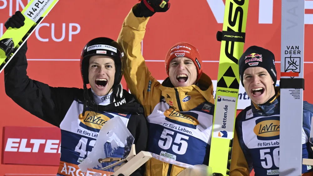 Winner Karl Geiger, center, from Germany celebrates on the podium next to second place, Gregor Deschwanden from Switzerland, left, and third place, Andreas Wellinger from Germany during the Nordic skiing/ski jumping World Cup, large hill men's second round in Klingenthal, Germany, Sunday, Dec. 10, 2023. (Hendrik Schmidt/dpa via AP)