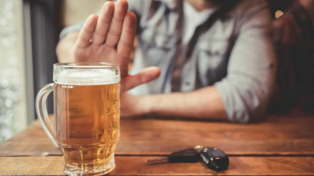 Do not drink and drive! Cropped image of man showing stop gesture and refusing to drink beer. Car keys lying near