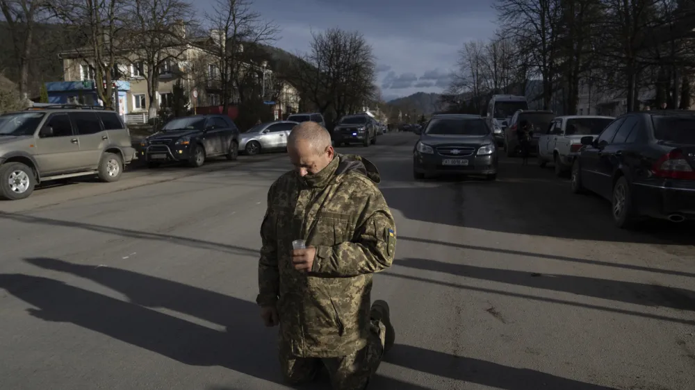 A Ukrainian serviceman kneels during the funeral ceremony of fallen comrade Vasyl Boichuk, killed in Mykolayiv in March 2022, in Verkhovyna, Ukraine, Tuesday, Dec. 26, 2023. (AP Photo/Evgeniy Maloletka)