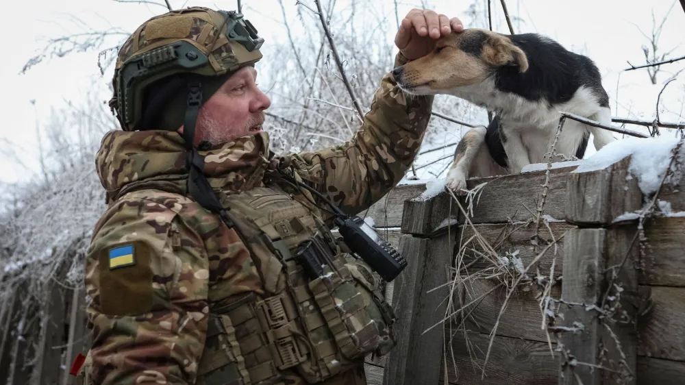 Artem, a serviceman of infantry battalion of the 61st mechanised brigade pets a dog in a trench at a position near the frontline, amid Russia's attack on Ukraine, in Kharkiv region, Ukraine January 6, 2024. REUTERS/Sofiia Gatilova