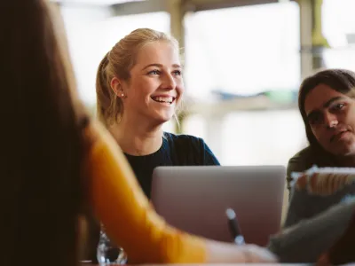 Female student sitting amongst classmates and smiling in lecture room. University students in classroom after lecture.