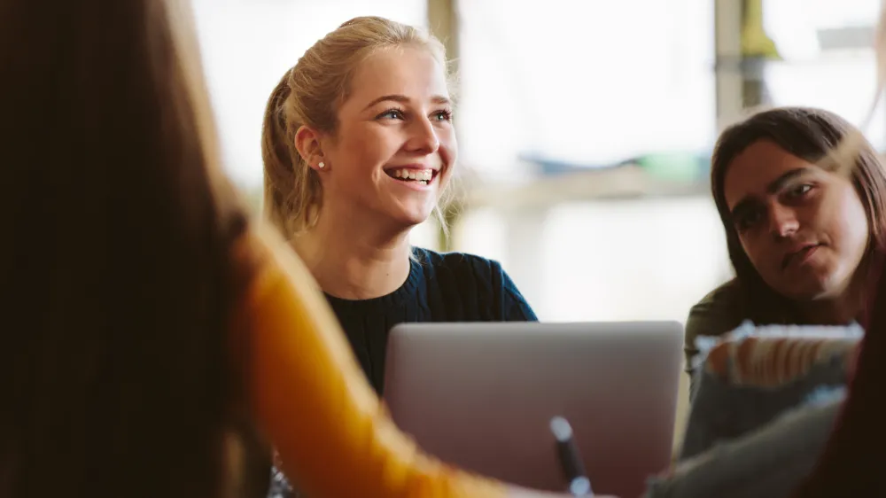 Female student sitting amongst classmates and smiling in lecture room. University students in classroom after lecture.