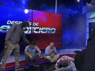 Oboroženi in zamaskirani moški v studiu telvizije TC ob novinarjih. Končalo se je brez strelov.