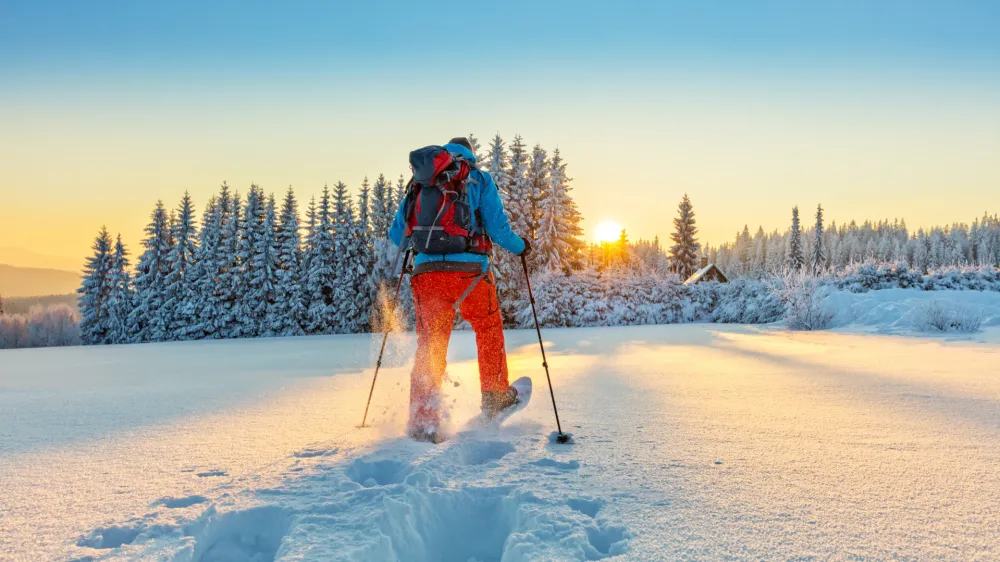Snowshoe walker running in powder snow with beautiful sunrise light. Outdoor winter activity and healthy lifestyle
