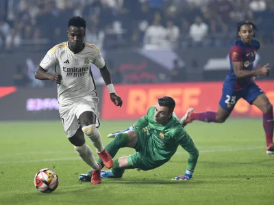Real Madrid's Vinicius Junior, left, passes through Barcelona's goalkeeper Inaki Pena during the Spanish Super Cup final soccer match between Real Madrid and Barcelona at Al-Awwal Park Stadium in Riyadh, Saudi Arabia, Sunday, Jan. 14, 2024. (AP Photo)