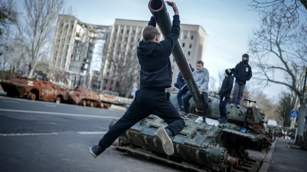 FILED - 25 February 2024, Ukraine, Mykolaiv: Children play on a destroyed Russian tank in front of the former headquarters of the regional administration of Mykolaiv oblast, after the visit of the German Foreign Minister. On March 29, 2022, the building was hit by Russian missiles and almost completely destroyed. Mykolaiv is an important port city near Odessa. Photo: Kay Nietfeld/dpa