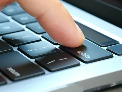 Finger of the computer user, he presses the delete button on the computer keyboard.
