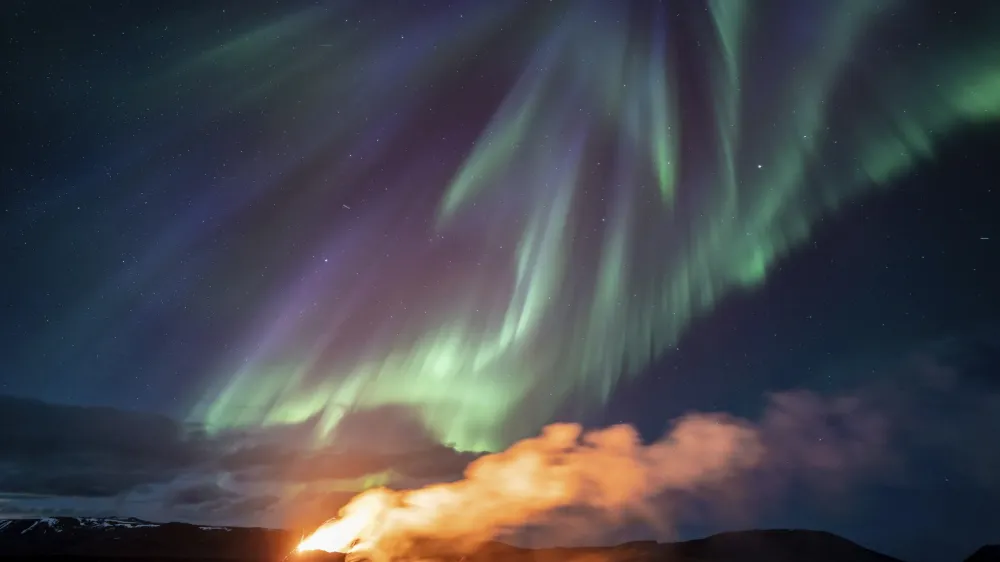 A view of the eruption area with the northern lights dancing in the sky near the town of Grindavik, Iceland, Tuesday April 16, 2024. The volcano in southwestern Iceland that erupted three times in December, January and February, sending lava towards a nearby community, keeps erupting. (AP Photo/Marco di Marco)