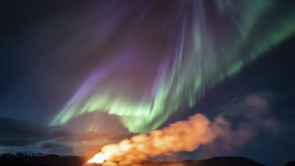 A view of the eruption area with the northern lights dancing in the sky near the town of Grindavik, Iceland, Tuesday April 16, 2024. The volcano in southwestern Iceland that erupted three times in December, January and February, sending lava towards a nearby community, keeps erupting. (AP Photo/Marco di Marco)