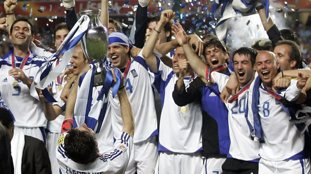 Greece players led by captain Theodoros Zagorakis (7) celebrate on the podium with the cup after winning the Euro 2004 soccer final in Lisbon July 4, 2004. Greece defeated host Portugal 1-0. REUTERS/Mike Finn-Kelcey GB/KC - RTRT6LD