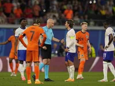 Referee Anthony Taylor is surrounded by players as he waits for a fourth official decision on a goal by Xavi Simons of the Netherlands that was then disallowed for offside during the Group D match between the Netherlands and France at the Euro 2024 soccer tournament in Leipzig, Germany, Friday, June 21, 2024. (AP Photo/Hassan Ammar)