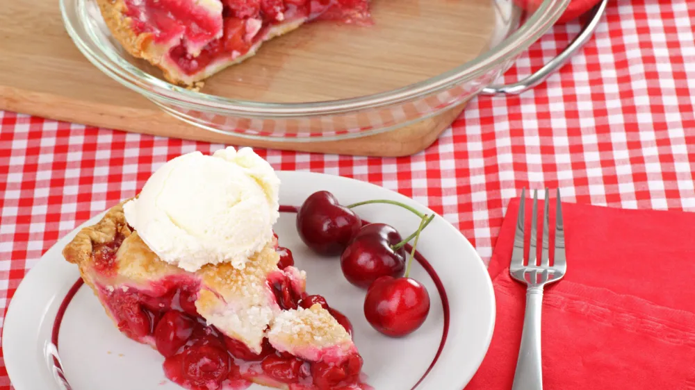 Slice of cherry pie with a scoop of ice cream on a plate