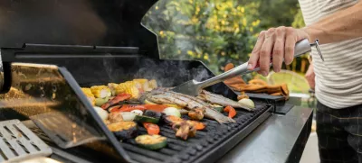 People grilling fish and corn on a modern grill outdoors at sunet, close-up. Cooking food on the open air / Foto: Rosshelen