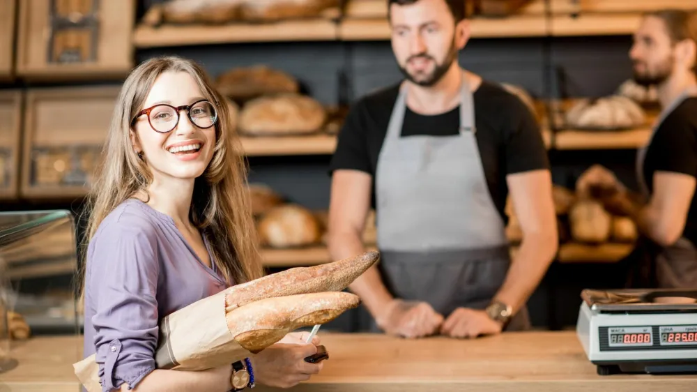 Portrait of a happy woman client buying bread at the bakery shop with handsome male sellers / Foto: Rosshelen
