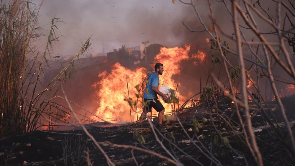 A volunteer tries to extinguish the fire in northern Athens, Monday, Aug. 12, 2024, as hundreds of firefighters tackle a major wildfire raging out of control on fringes of Greek capital. (AP Photo/Aggelos Barai)