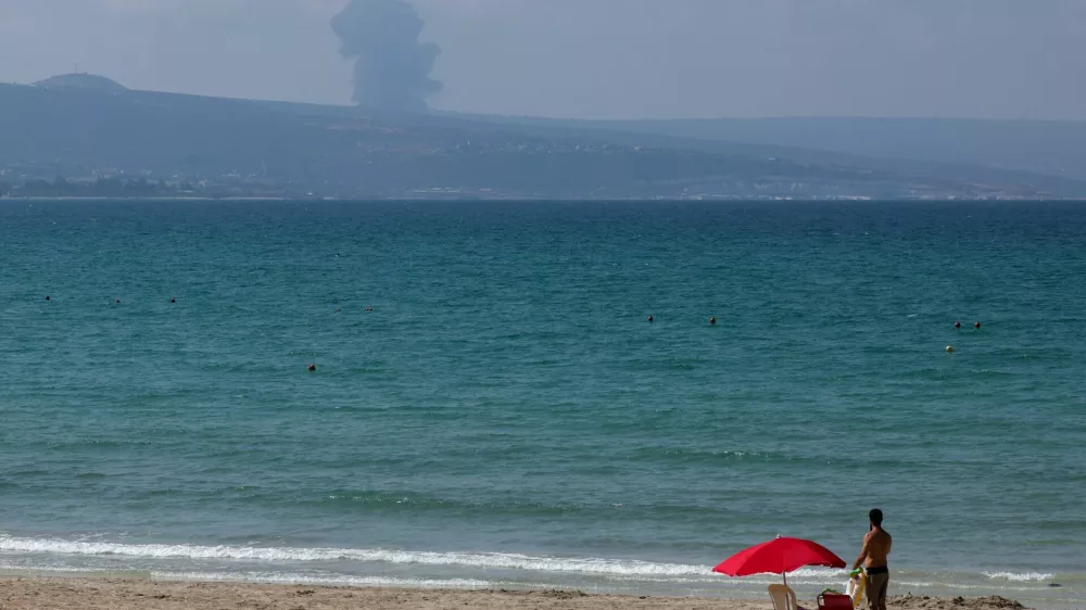 A view shows smoke on the Lebanese side of the border with Israel, as a man stands at a beach in Tyre, amid ongoing cross-border hostilities between Hezbollah and Israeli forces, southern Lebanon August 25, 2024. REUTERS/Aziz Taher