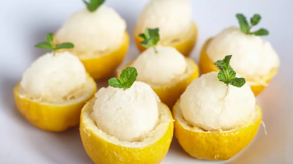 Lemon sorbet or ice cream inside fresh lemons decorated with mint leaves on big white plate / Foto: Alexbai
