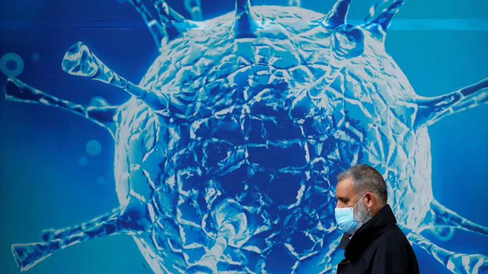 FILE PHOTO: A man wearing a protective face mask walks past an illustration of a virus outside a regional science centre, as the city and surrounding areas face local restrictions in an effort to avoid a local lockdown being forced upon the region, amid the coronavirus disease (COVID-19) outbreak, in Oldham, Britain August 3, 2020. REUTERS/Phil Noble/File Photo