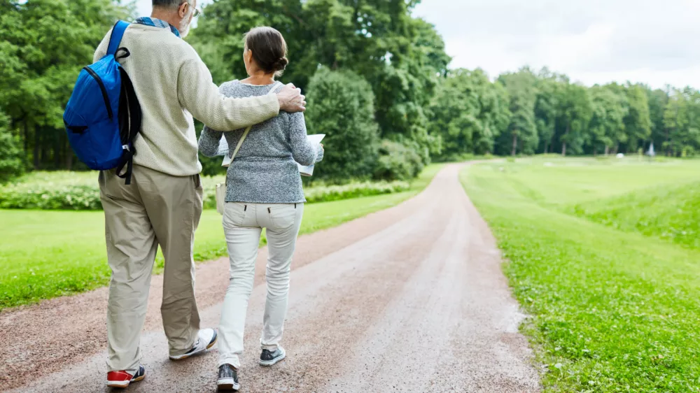Affectionate retired backpackers moving down country road / Foto: Shironosov
